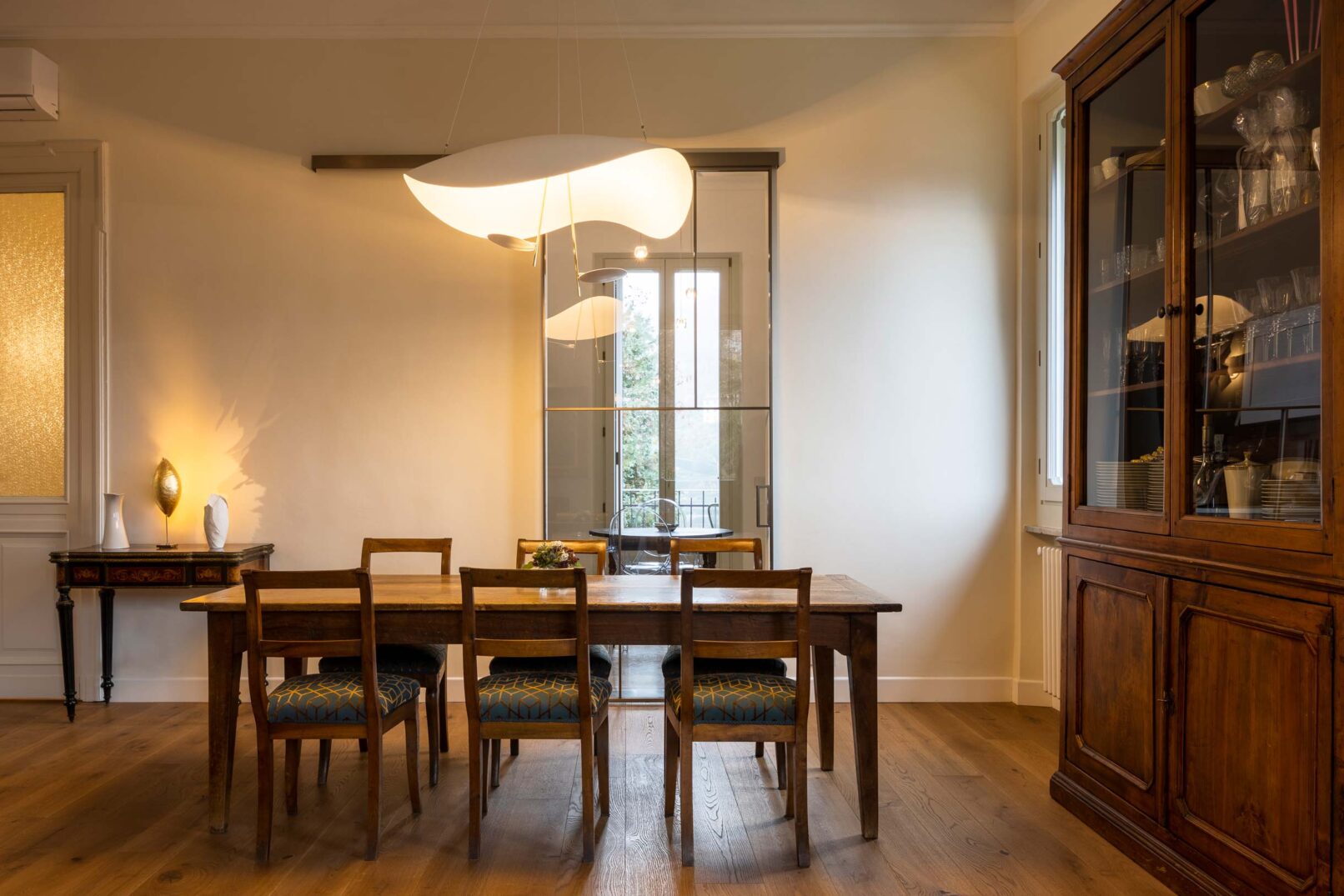 sala da pranzo con tavolo e sedie in legno stile arte povera con corpo illuminante sospeso